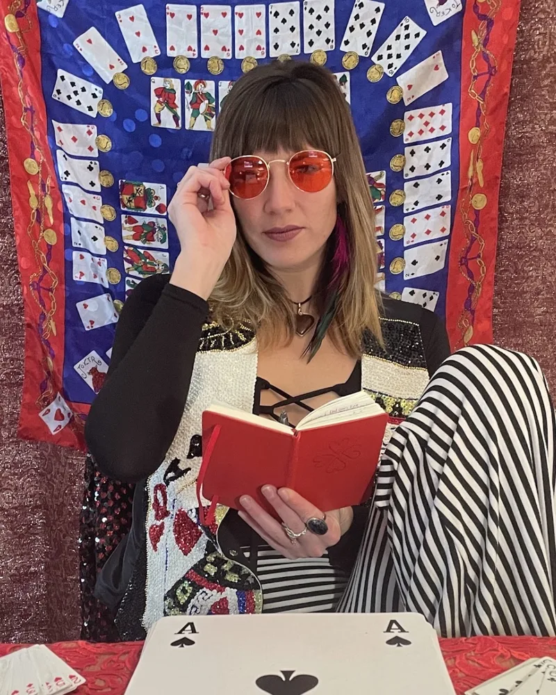 Katie, the Card Lady, at her reading table with a notebook and an oversized Ace of Spades